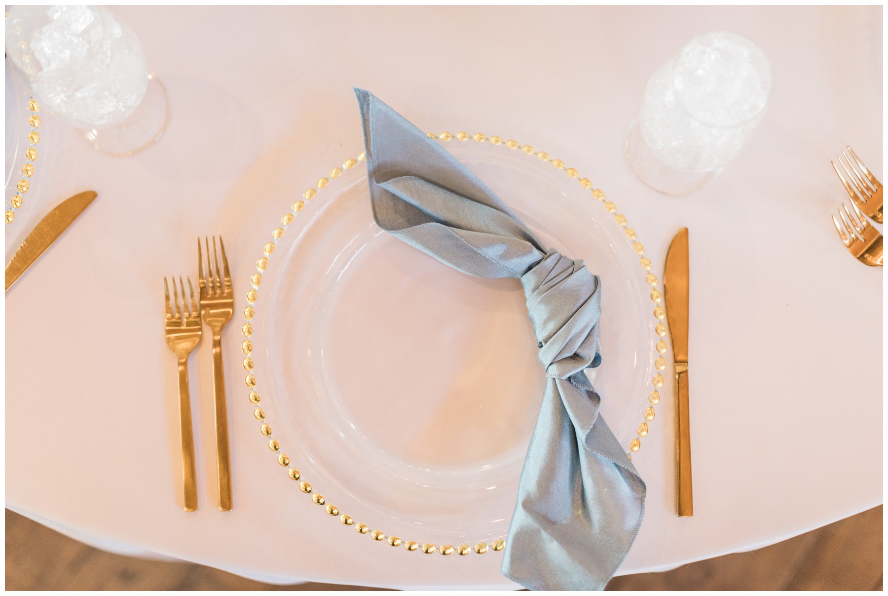 White satin tablecloths, powder blue satin napkins, and gold beaded chargers for a spring wedding reception